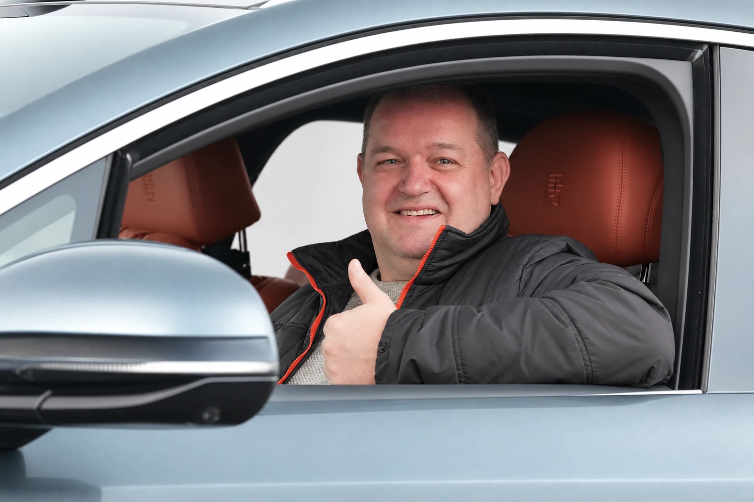 BYD Tang L, mężczyzna siedzący za kierownicą z uniesionym kciukiem przy otwartym oknie.