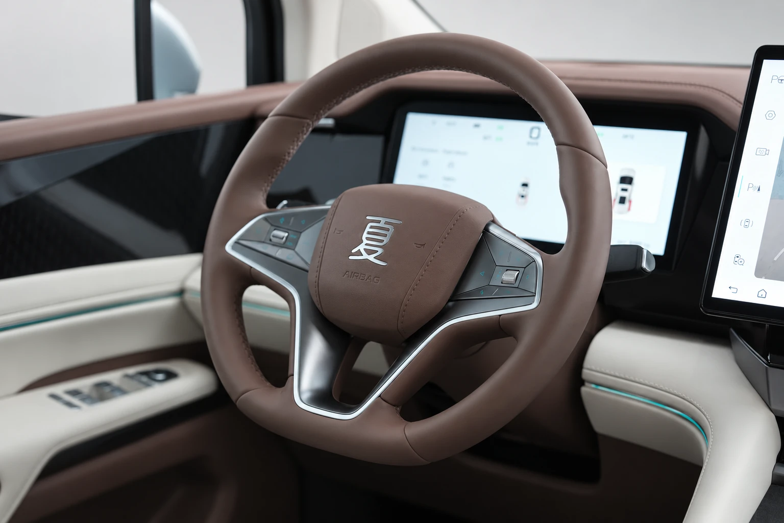 BYD Xia, zbliżenie na brązową kierownicę z emblematem i cyfrowymi wskaźnikami w tle.