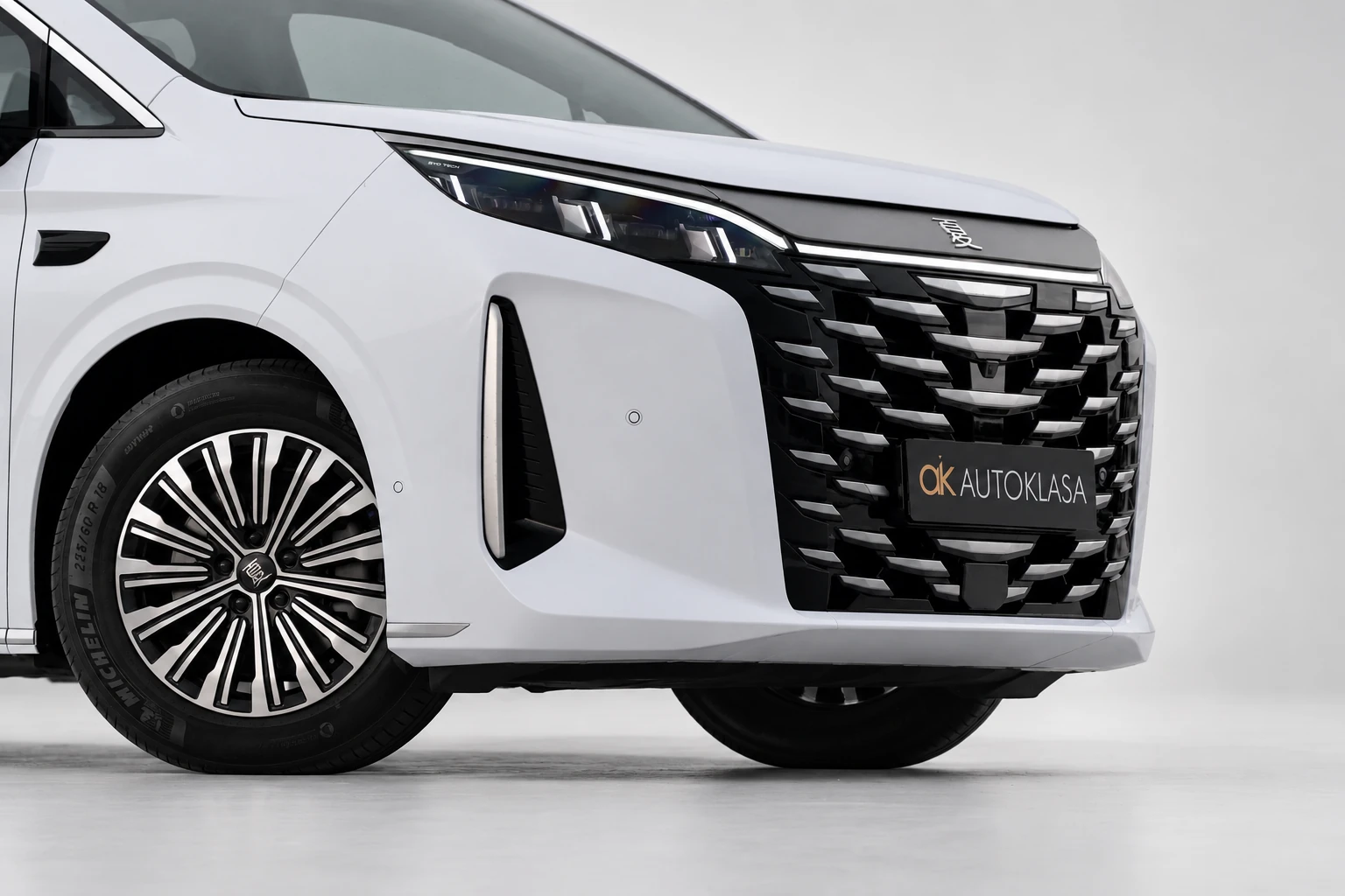 BYD Xia, zbliżenie na duży grill, przednie koło i dolną krawędź białego zderzaka.