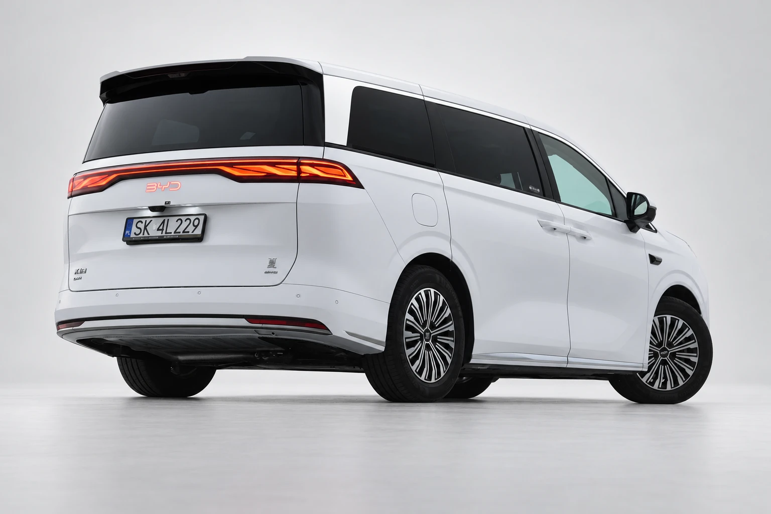 BYD Xia od tyłu i drugiego boku, z czerwoną listwą lamp, ciemnymi szybami i białym nadwoziem; ujęcie 6.