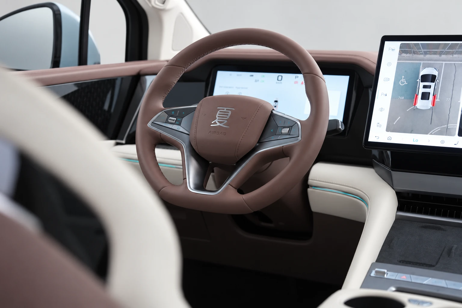 BYD Xia, kierownica i ekrany kokpitu oglądane spomiędzy oparć przednich foteli.