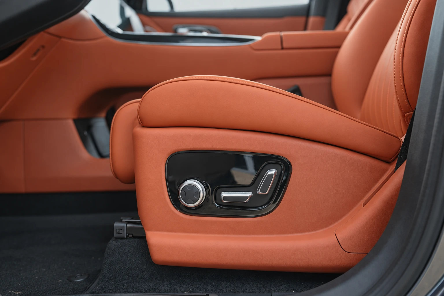 Panel sterowania fotela Geely Galaxy M9 pod pomarańczowym podłokietnikiem.