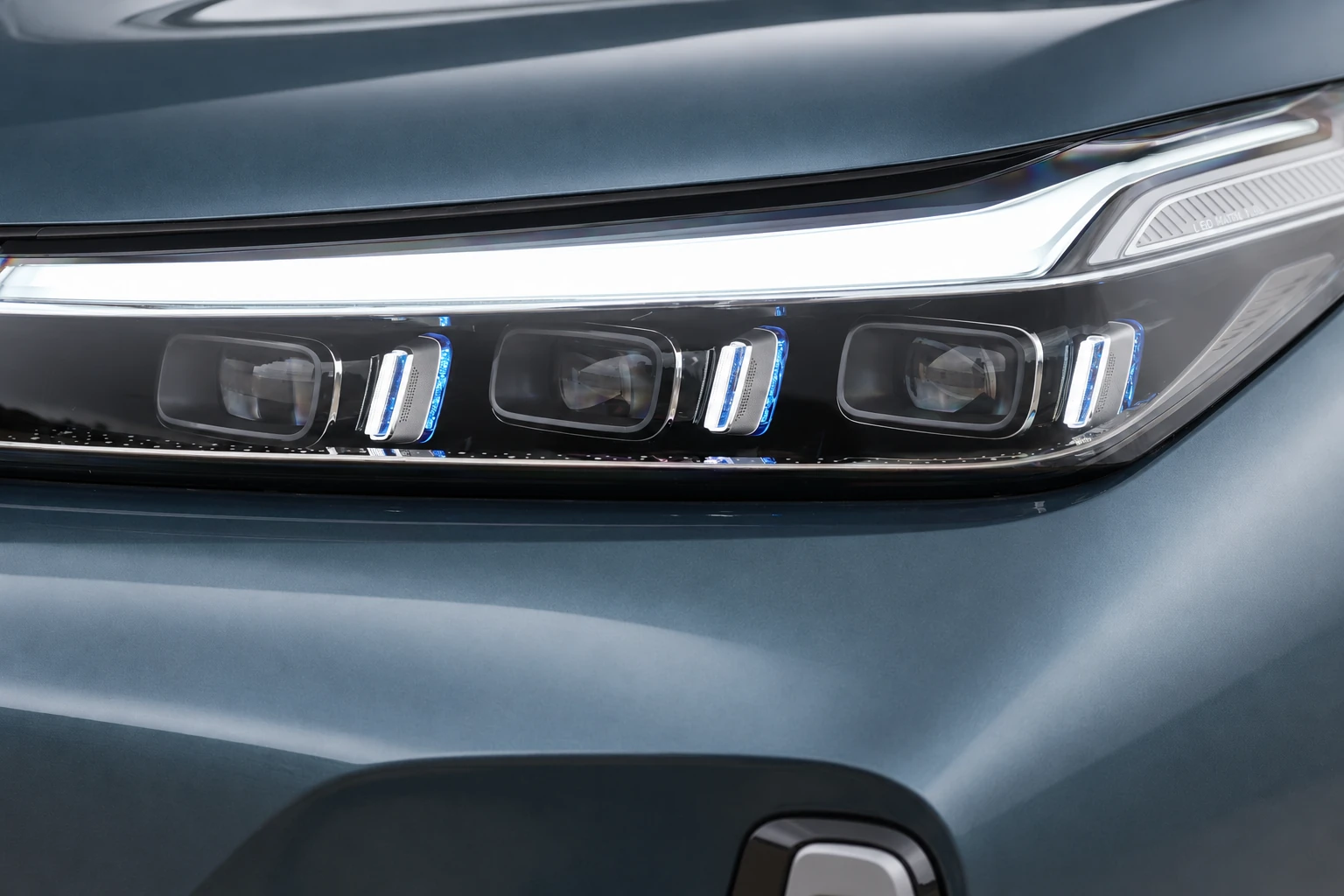 Zbliżenie przedniego reflektora Geely Galaxy M9 z listwą świetlną i trzema segmentami lampy.